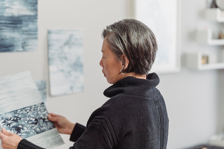 A woman in a black sweater examines abstract artwork in her studio, showcasing her creative process.